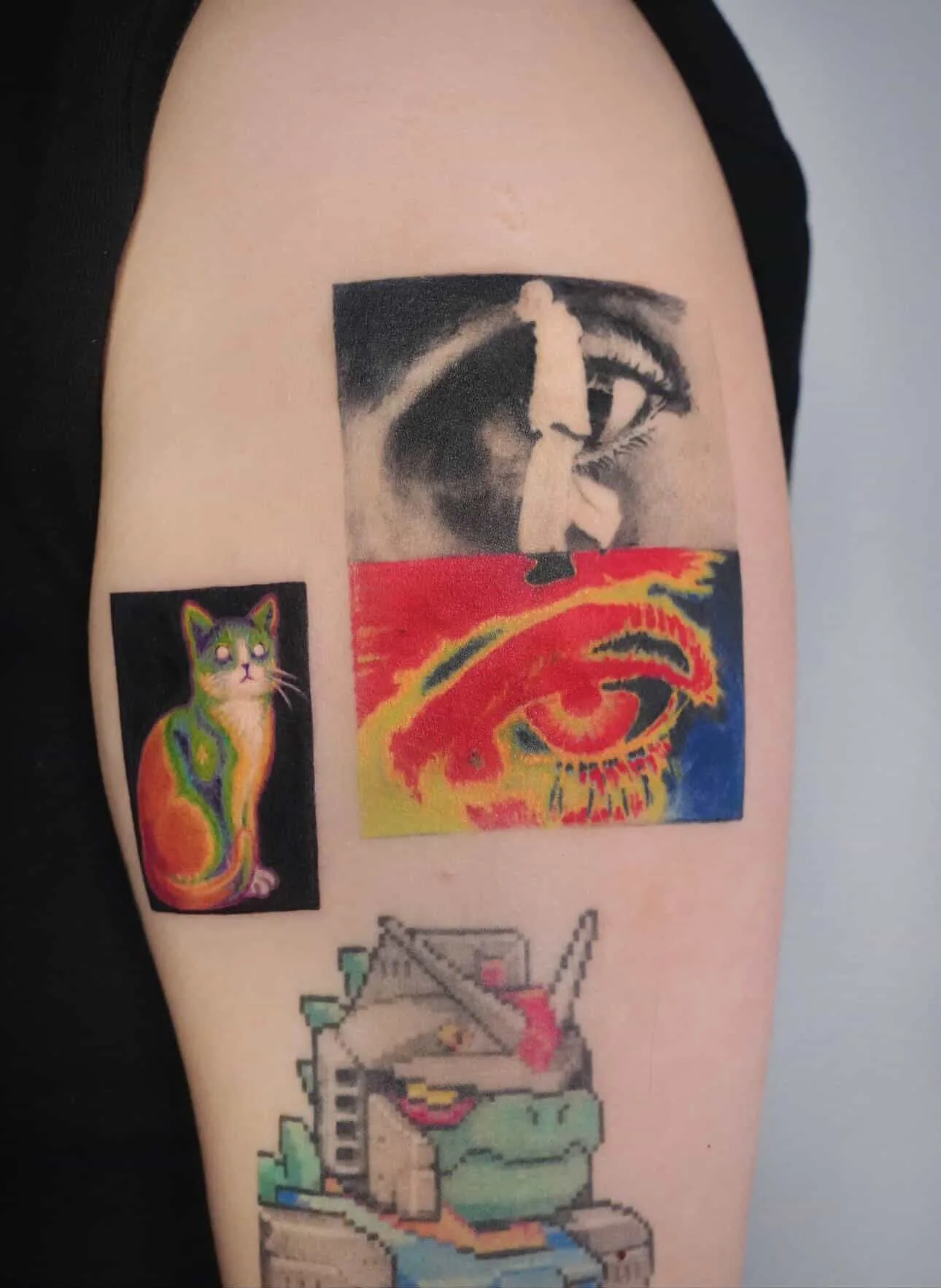 Client's upper arm carrying finished colour tattoos — psychedelic cat, portrait collage and pixel-art scene