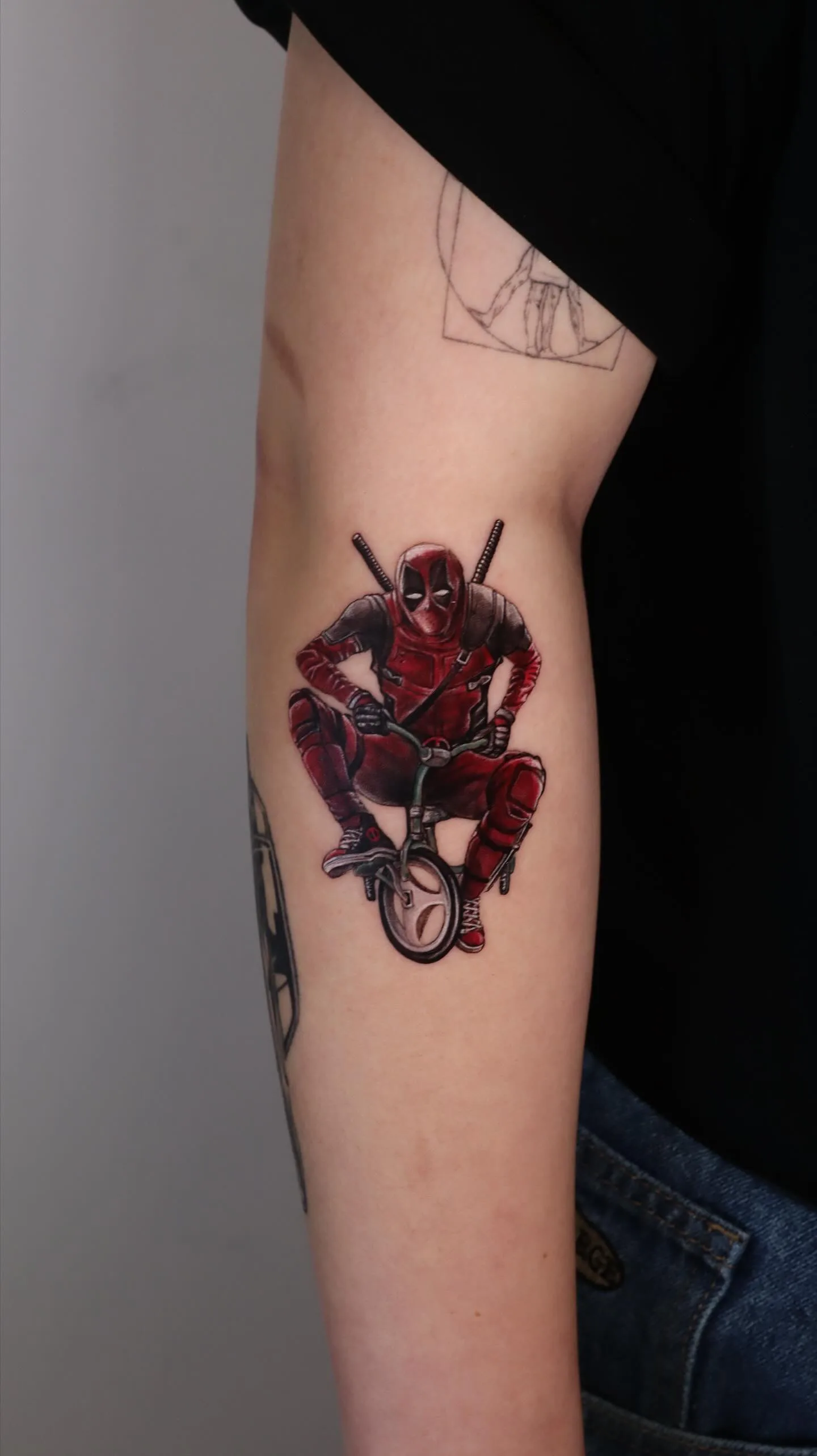 Forearm with colour-realism Deadpool tattoo and fine-line sketch pieces
