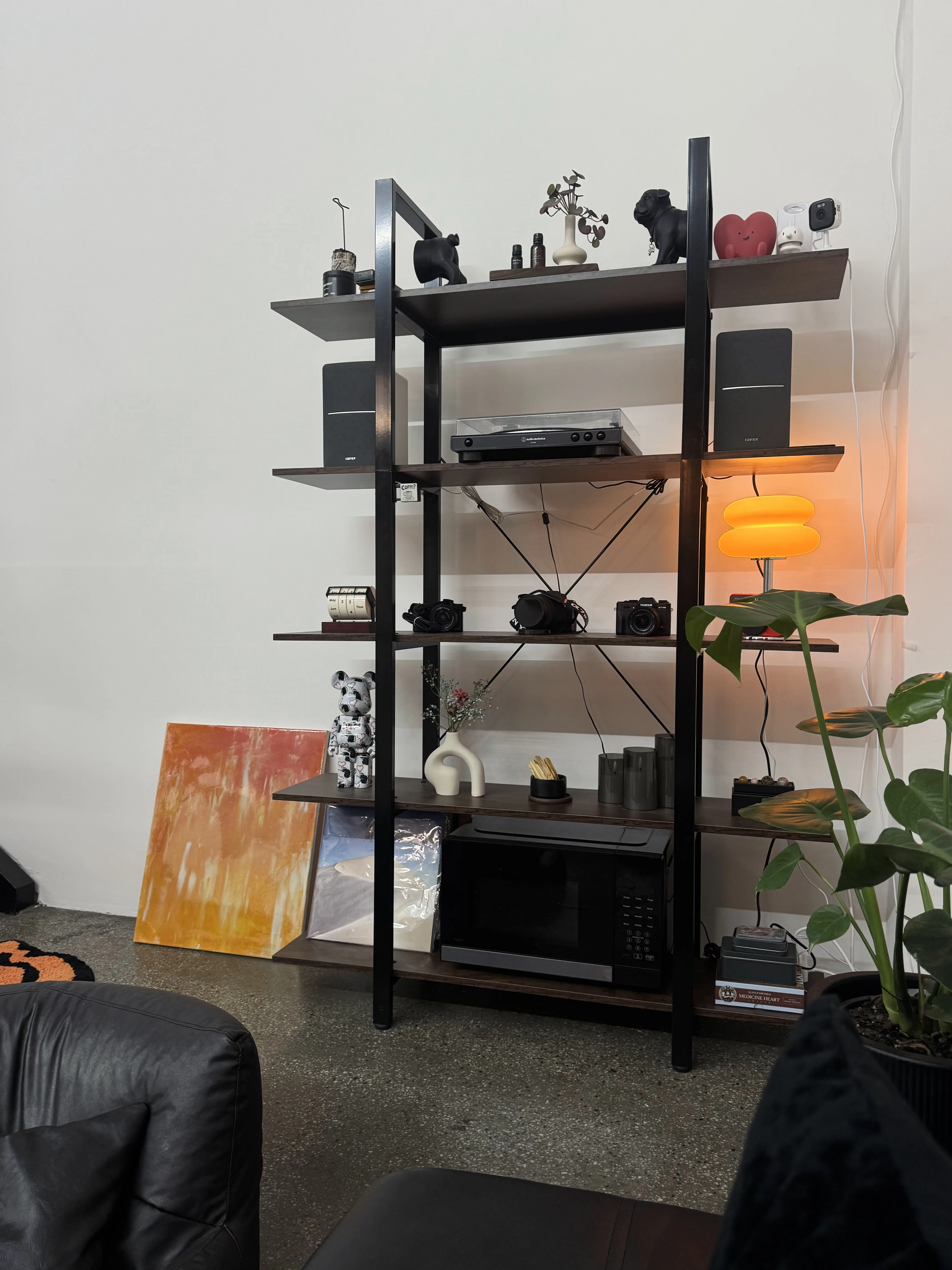 Curated studio shelf — record player, speakers, warm lamp, plants and a leather couch in the foreground